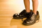 Big shoes to fill, child's feet in large black shoes, on wood fl